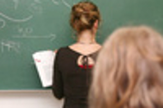 Eine Lehrerin steht vor einer Tafel und schreibt, Schüler sehen zu